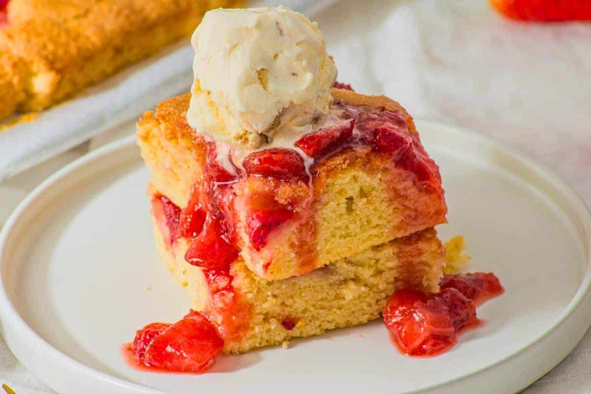 Two pieces of yellow morning cake topped with strawberry sauce and a scoop of vanilla ice cream are stacked on a white plate, making for an indulgent special breakfast treat.