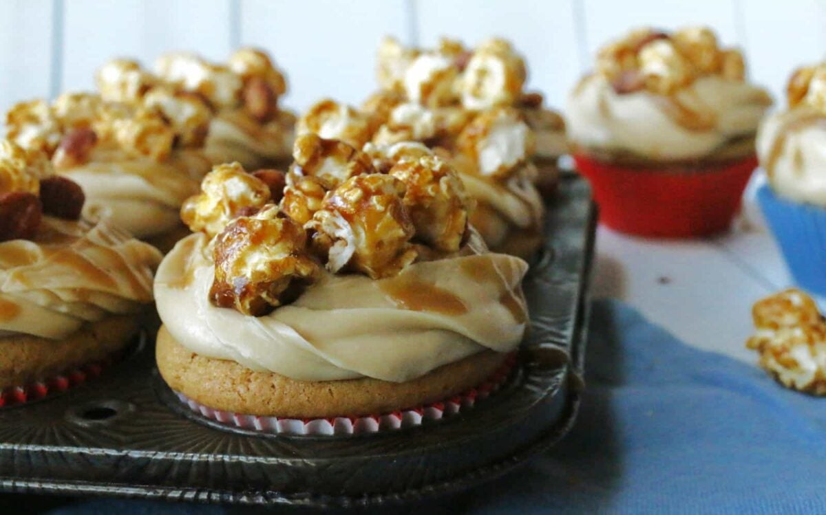 Cupcakes topped with caramel frosting and caramel popcorn, arranged in a baking tray with a few on the side—perfect as celebration cakes or for anyone who loves decadent cakes.