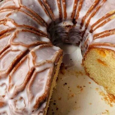 A Bundt cake with white glaze, partially sliced to reveal its moist, yellow interior dotted with fruit—perfect for celebration cakes—presented on a round ceramic plate.