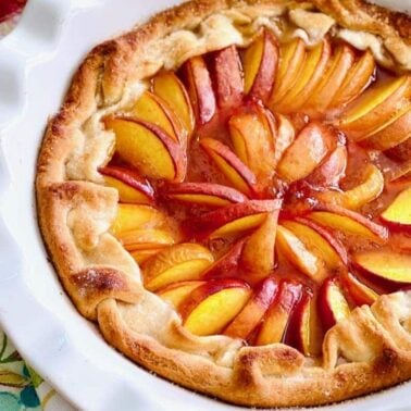 A rustic peach galette with golden crust and sliced peaches arranged in a circular pattern, served in a white pie dish—one of our easy recipes perfect for sweet and savory recipes lovers alike.