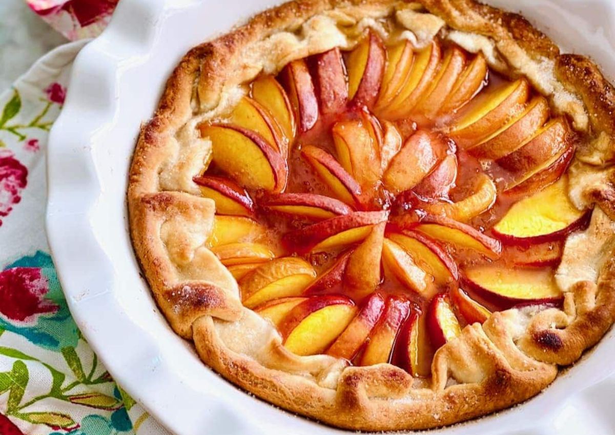 A rustic peach galette with golden crust and sliced peaches arranged in a circular pattern, served in a white pie dish—one of our easy recipes perfect for sweet and savory recipes lovers alike.