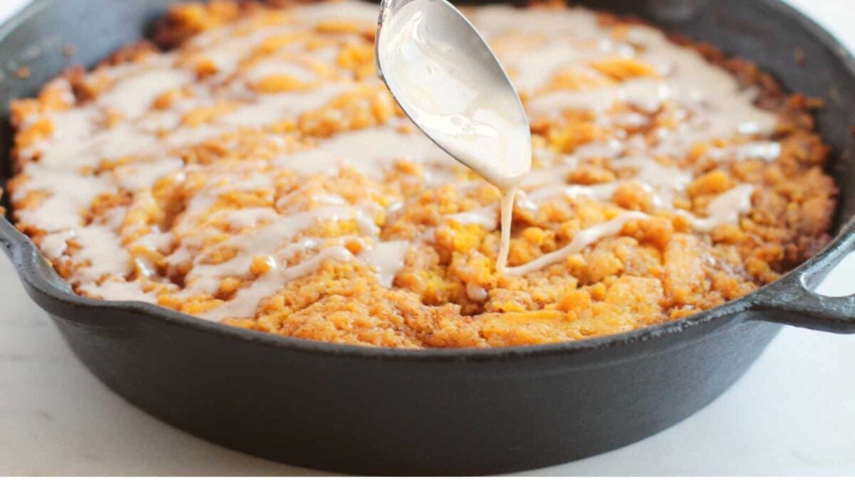 A spoon drizzles icing over a baked dessert in a black cast iron skillet, creating one of those stunning desserts perfect for any occasion.