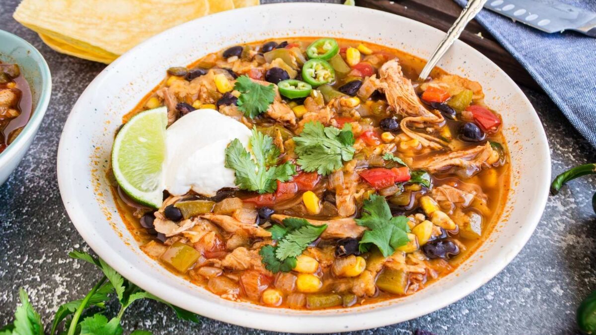 A bowl of hearty chicken tortilla soup with black beans, corn, diced tomatoes, sliced jalapeños, fresh cilantro, and a lime wedge—perfect for those seeking hearty soups or delicious dairy-free recipes.