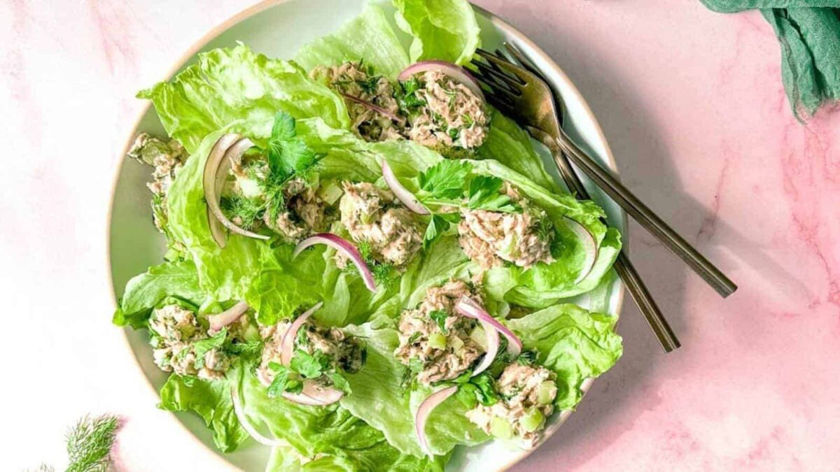 Plate of lettuce wraps filled with tuna salad, garnished with red onion slices and herbs—an easy addition to your collection of fresh tuna recipes. Two forks rest on the side, ready to enjoy.