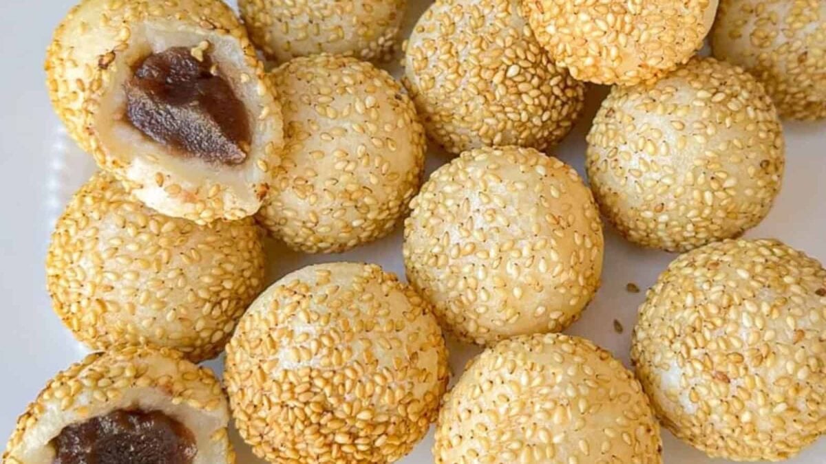 Round sesame seed balls with a golden exterior, some shown with a red bean paste filling inside, arranged on a white surface—perfect for those seeking satisfying recipes and delicious egg-free treats.