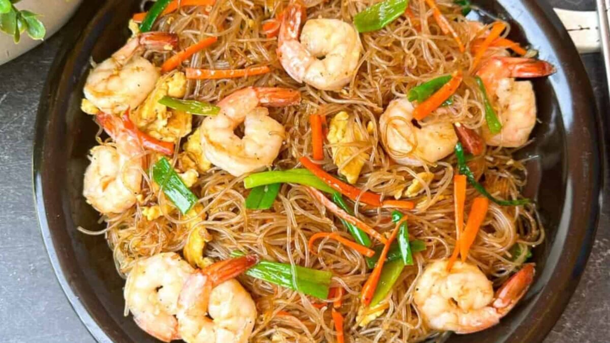 A black plate filled with stir-fried glass noodles, shrimp, sliced carrots, green onions, and scrambled egg—perfect for those seeking delicious gluten-free recipes.