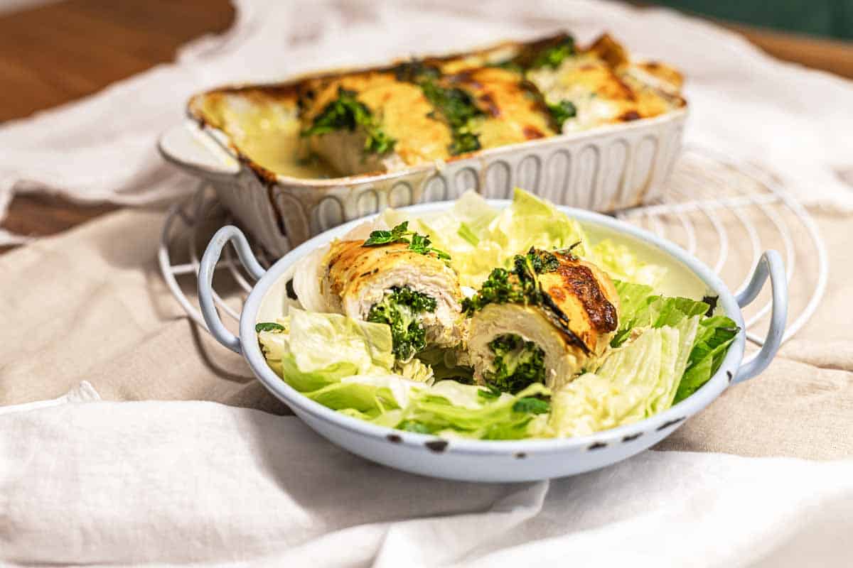 A dish of stuffed chicken breasts with greens, sliced and served on a bed of lettuce, with more stuffed chicken in a baking dish in the background—a perfect choice for family meals or those who love classic chicken casseroles.