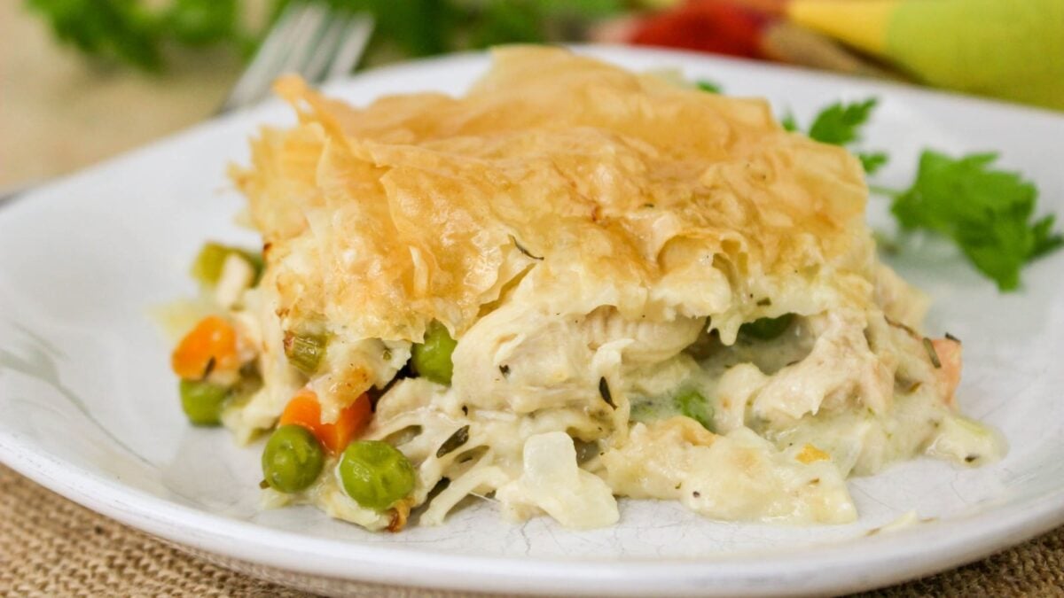 A serving of creamy vegetable and chicken casserole with savory pie filling is topped with flaky pastry and placed on a white plate.