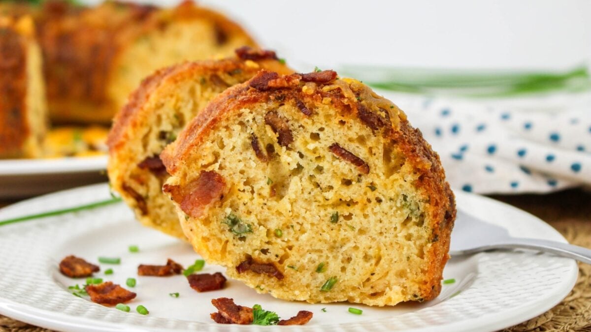 Two slices of savory bundt bread with visible bacon pieces and chives on a white plate, garnished with extra chives and bacon—perfect for easy breakfast recipes or special weekend breakfasts.