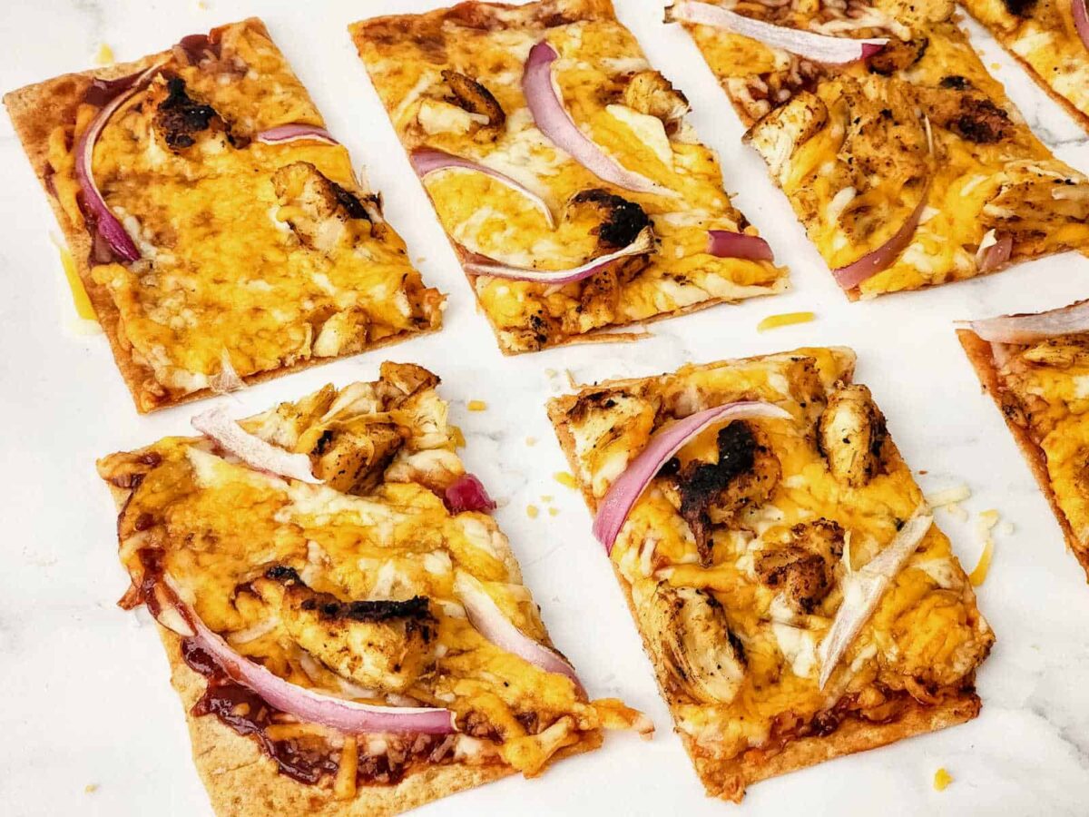 Rectangular slices of flatbread pizza topped with melted cheese, grilled chicken pieces, and red onion strips showcase one of our unique pizzas on a white surface.