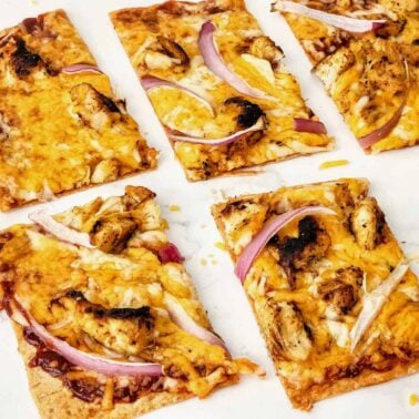 Rectangular slices of flatbread pizza topped with melted cheese, grilled chicken pieces, and red onion strips showcase one of our unique pizzas on a white surface.
