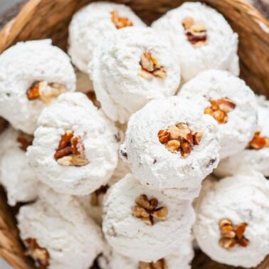 A basket filled with round, powdered sugar-covered cookies, each topped with a walnut piece—perfect for fans of old fashioned dessert recipes.