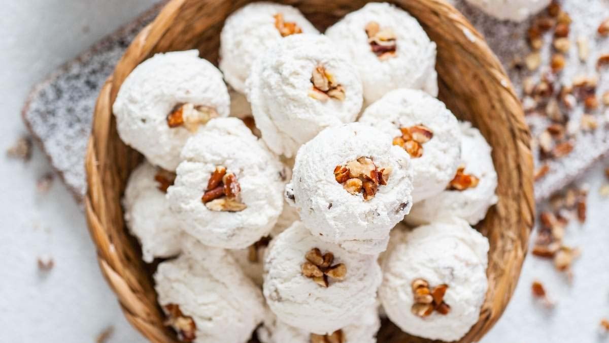 A basket filled with round, powdered sugar-covered cookies, each topped with a walnut piece—perfect for fans of old fashioned dessert recipes.