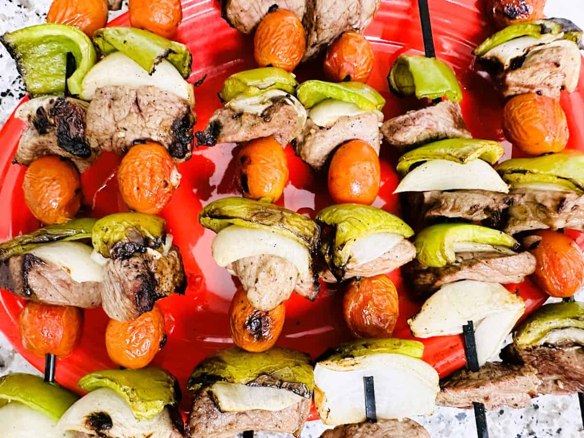 Skewers with grilled beef, green bell peppers, onions, and cherry tomatoes arranged on a red plate—perfect for flavorful BBQ dinners that won't set off your smoke alarm.