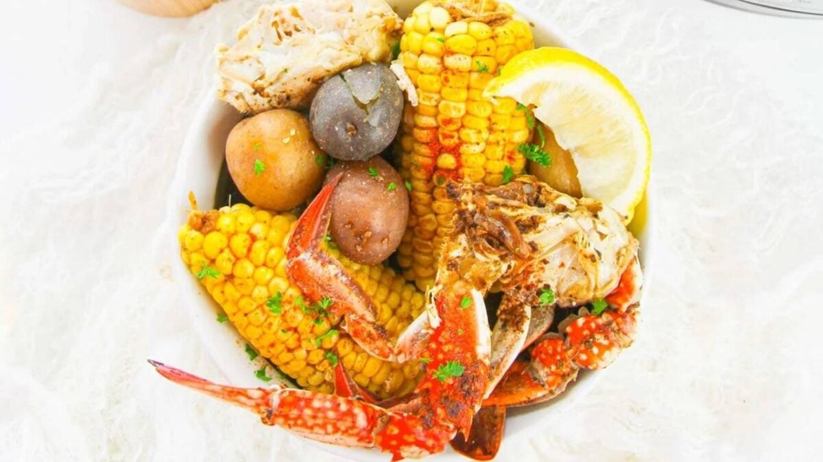 A bowl containing crab legs, corn on the cob, small potatoes, a lemon wedge, and parsley garnish—perfect for easy dinner nights and those who love quick recipes.