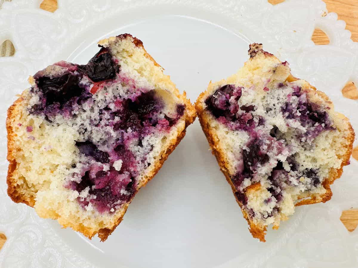 A blueberry muffin split in half on a white plate, showing a moist interior with visible blueberries—perfect inspiration for blueberry breakfast recipes and new breakfast ideas.