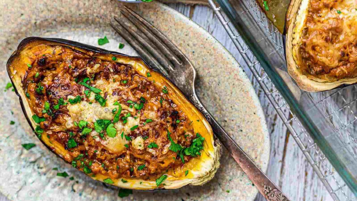 A baked stuffed eggplant half filled with a vegetable mixture, topped with melted cheese and chopped herbs, served on a plate with a fork—perfect for dinner or as a standout among your favorite eggplant dishes.