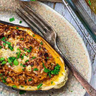 A baked stuffed eggplant half filled with a vegetable mixture, topped with melted cheese and chopped herbs, served on a plate with a fork—perfect for dinner or as a standout among your favorite eggplant dishes.