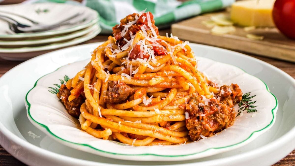A plate of spaghetti with tomato meat sauce, topped with grated cheese, sits on a white and green dish, offering rich flavor inspired by classic sauce recipes.