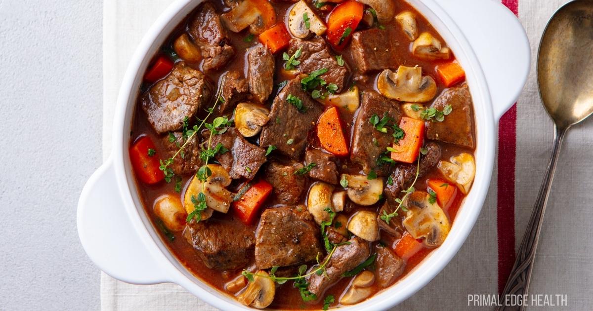A white bowl filled with beef stew containing chunks of beef, sliced mushrooms, carrots, and garnished with fresh herbs—a comforting choice for easy beef recipes or cozy dinner recipes.