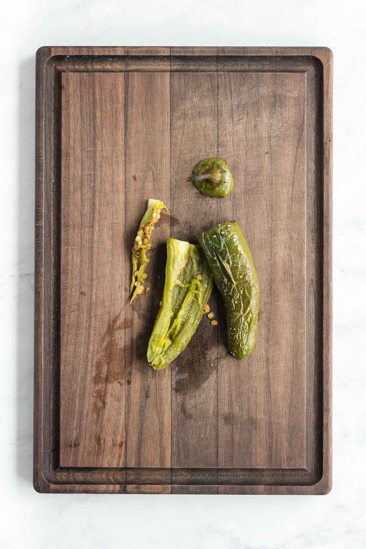 A roasted poblano pepper, partly peeled and seeded, sits on a wooden cutting board.