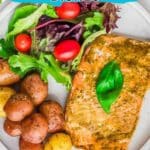 A plate with baked salmon, small roasted potatoes, and a salad with greens and cherry tomatoes. Text overlay reads "11 Baked Seafood Dishes.