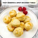 A plate of round, golden biscuits with a few raspberries on the side, displayed on a white plate with a blue rim. Text above reads: "11 Biscuits That Deserve a Spot on Every Table.
