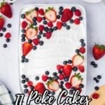 Rectangular cake topped with whipped cream, sliced strawberries, blueberries, and raspberries in a white dish, surrounded by fresh berries and a wooden spatula on a light surface.