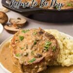 A plate with a pork chop covered in gravy, served with mashed potatoes and garnished with herbs; skillet and mushrooms in the background.