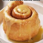 A large cinnamon roll with thick icing sits on a white plate, accompanied by text promoting Serious Cinnamon Rolls packed with generous filling.