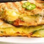 Close-up of a grilled sandwich with melted cheese, tomato, and jalapeño slices, stacked on a white plate. Text reads "12 Sandwiches That Refuse To Be Ordinary.