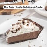 A slice of chocolate cream pie with whipped topping and chocolate shavings on a white plate, with a fork and more pie in the background.