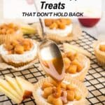 A hand drizzles caramel sauce over a caramel apple dessert topped with diced apples, with more desserts and apple slices in the background.