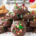 A stack of chocolate-covered cookies decorated with colorful sprinkles sits on a white surface with peanut butter and holiday decorations in the background. Text reads: "14 Easy Ways to Coat It in Chocolate and Call It Dessert.