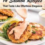 A hand pours creamy sauce over two salmon cakes on a white plate with arugula and lemon slices, next to a bowl of sauce and another plate of salmon cakes.