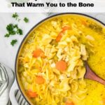 A pot of chicken noodle soup with carrots and noodles sits on a table next to a striped cloth and chopped parsley. Text reads “14 Soups and Stews That Warm You to the Bone.”.