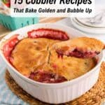 A dish of baked fruit cobbler with a golden crust sits on a woven mat; one serving is being lifted out, and fresh strawberries are nearby. Text above reads, "15 Cobbler Recipes.