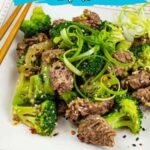 A plate of stir-fried beef with broccoli garnished with green onions, presented with chopsticks. Text overlay reads "14 Low-Carb Dinner Ideas"—perfect for anyone seeking delicious low-carb dinner ideas.