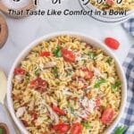 A large bowl of rotini pasta mixed with shredded chicken, grape tomatoes, and herbs sits on a marble surface, surrounded by ingredients and utensils. Text reads: “15 Pasta Dishes.”.