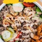 A bowl filled with ground beef, sliced cucumbers, cherry tomatoes, caramelized onions, and a creamy dressing, with a side of sweet potato fries. Text overlay promotes 15 bowl recipes.