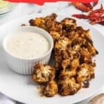 A plate of roasted cauliflower served with a bowl of creamy dipping sauce is shown. Text on the image reads: "15 Roasted Recipes That Taste Like Home.