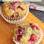 Two cranberry muffins in white paper liners sit on a wooden board, with text above reading “16 Fall Recipes That Bring Cozy Comfort to the Table.”.