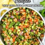 A bowl of chopped Mediterranean salad with tomatoes, cucumbers, onions, and parsley on a table, surrounded by fresh ingredients.