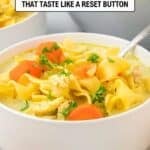 A bowl of chicken noodle soup with wide noodles, carrots, parsley, and a spoon, with text reading "16 Soups That Taste Like a Reset Button.