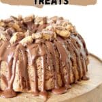 A bundt cake topped with chopped peanut butter cups and drizzled with chocolate sits on a wooden cake stand. Text above reads, “17 Peanut Butter Treats.”.