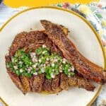 A plate with sliced smoked beef garnished with chopped onions and herbs, featured on a table with a floral napkin. Text reads, "11 Smoked Recipes That Pair Heat, Smoke, and Spice.