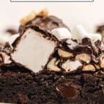 Close-up of a brownie topped with large marshmallows, chopped nuts, and chocolate drizzle on a plate. Text overlay reads "18 Brownies That Are Fudgy, Gooey, and Full of Flavor.