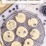 Nine lemon blueberry cookies cool on a wire rack, surrounded by blueberries, lemon slices, and baking ingredients. Text overlay reads “18 Lemon Recipes That Wake Up Your Taste Buds.”.