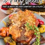 A plate with a cooked pork chop garnished with herbs, surrounded by roasted peppers and onions, sits on a table with a fork and knife nearby.