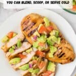 Grilled chicken breast topped with diced avocado, tomato, and onion salsa on a white plate, with a partial bowl of salad in the background.